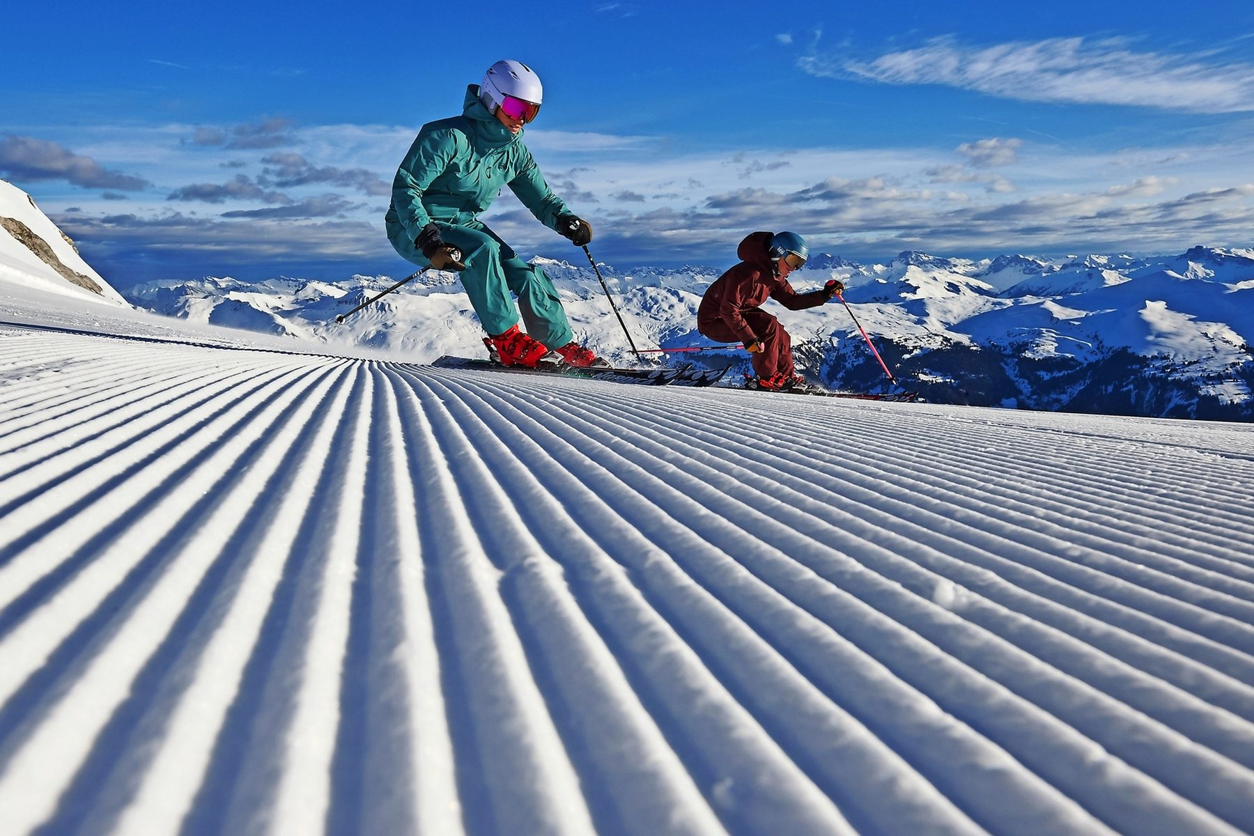 Zwei Skifahrende auf frisch präparierter Piste im Morgenlicht